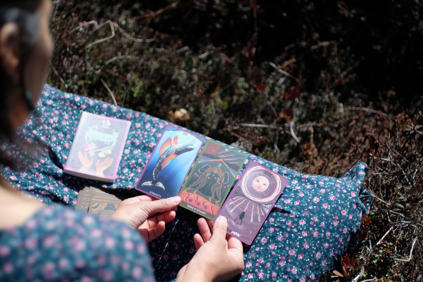 Person sitting outdoors with tarot cards on a floral-patterned fabric